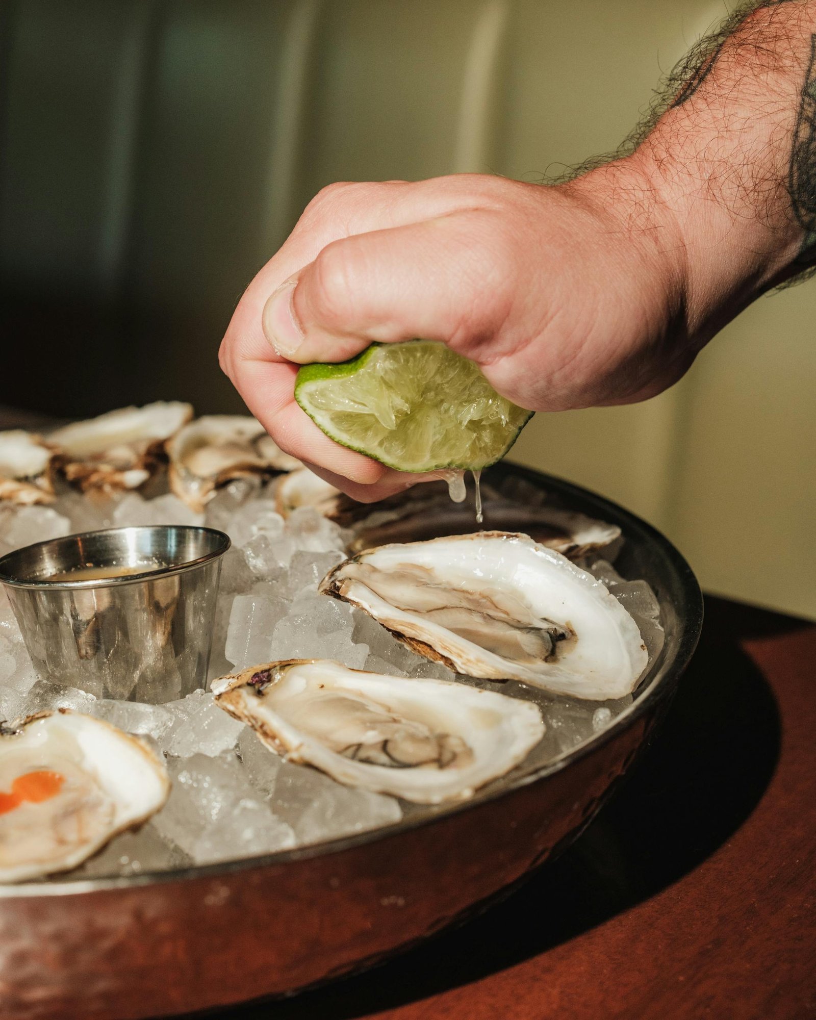 A hand squeezing lime over fresh oysters on ice, showcasing gourmet seafood preparation.