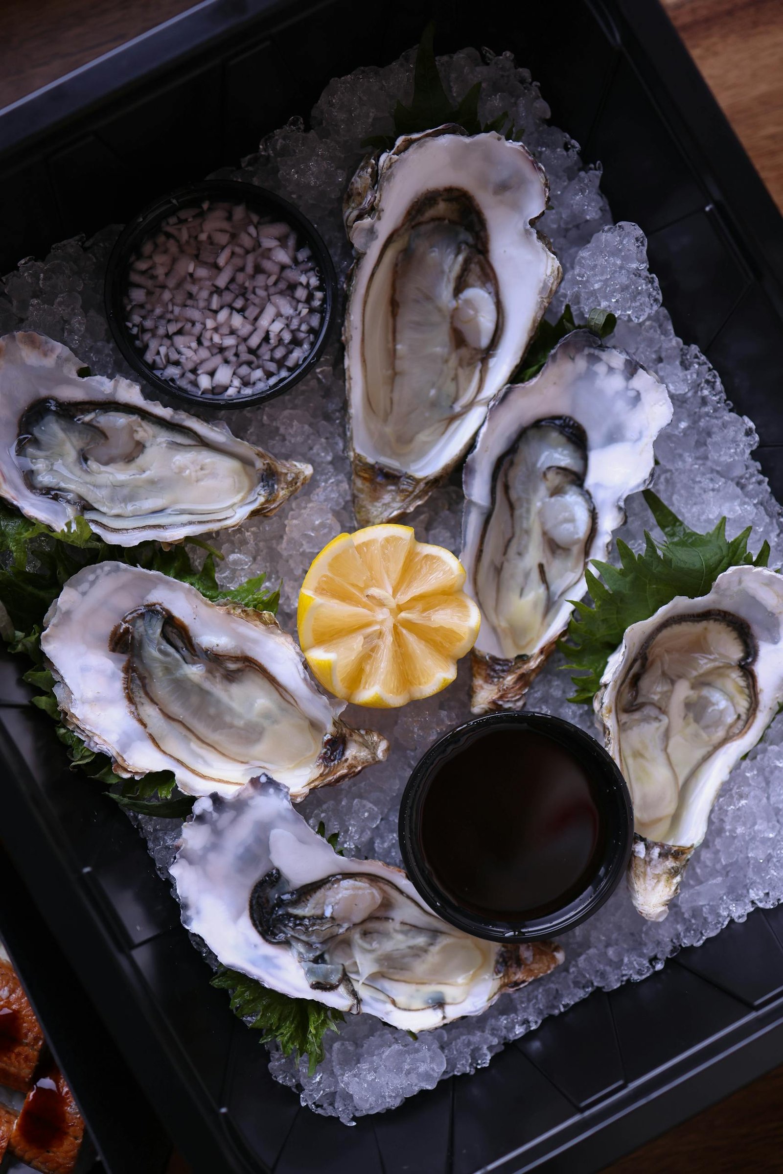 A platter of fresh oysters on ice garnished with a lemon slice, ideal for seafood lovers.