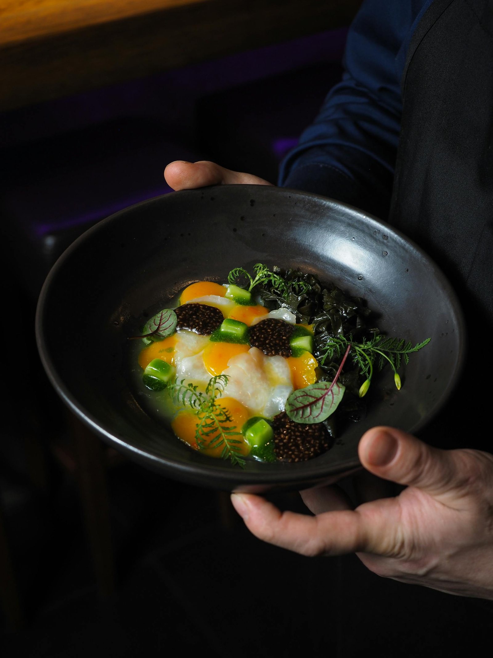 Close-up of a chef holding a gourmet dish with egg yolk and caviar.