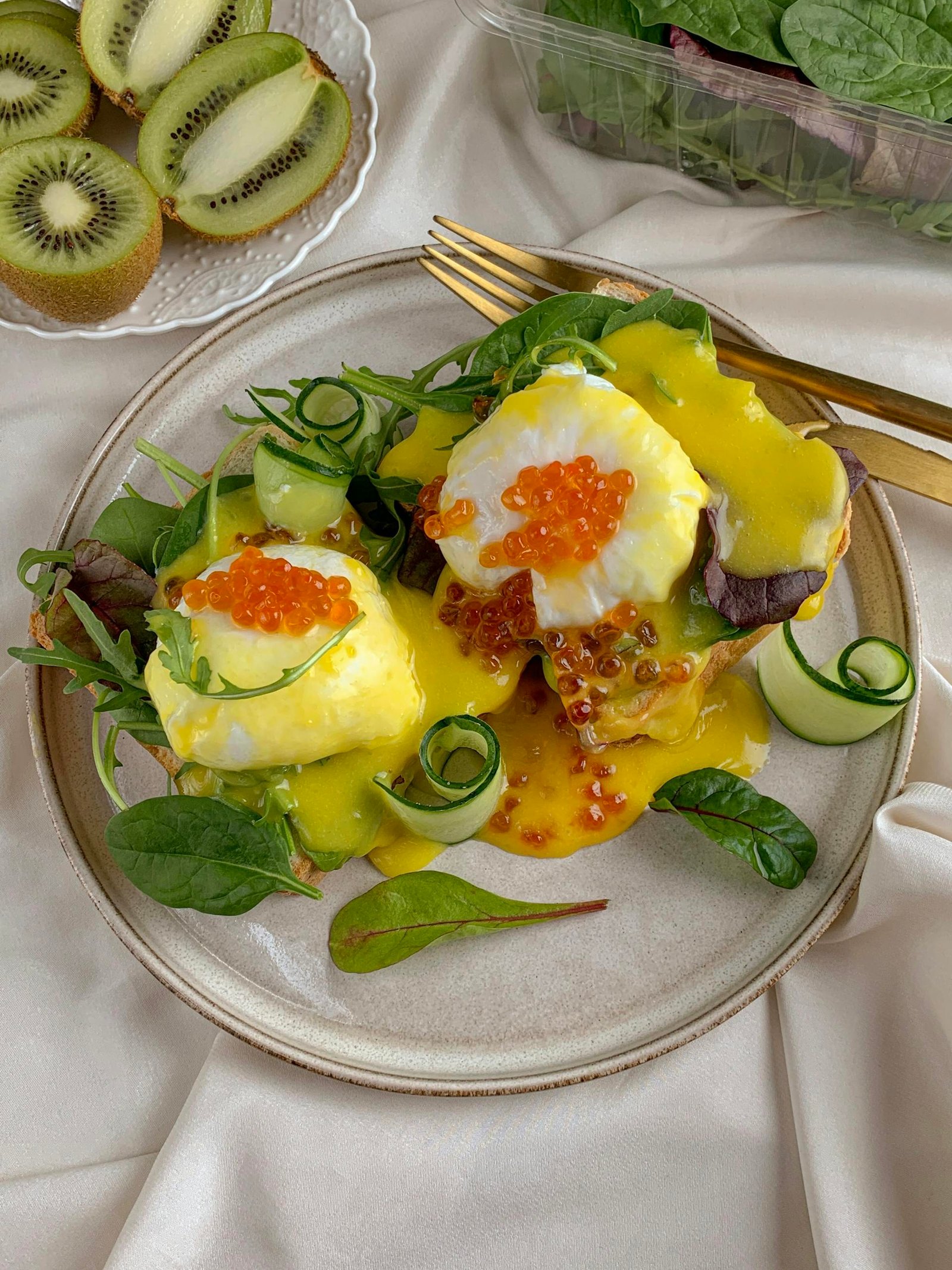 Delicious eggs benedict with caviar, spinach, and cucumber slices on a white plate.