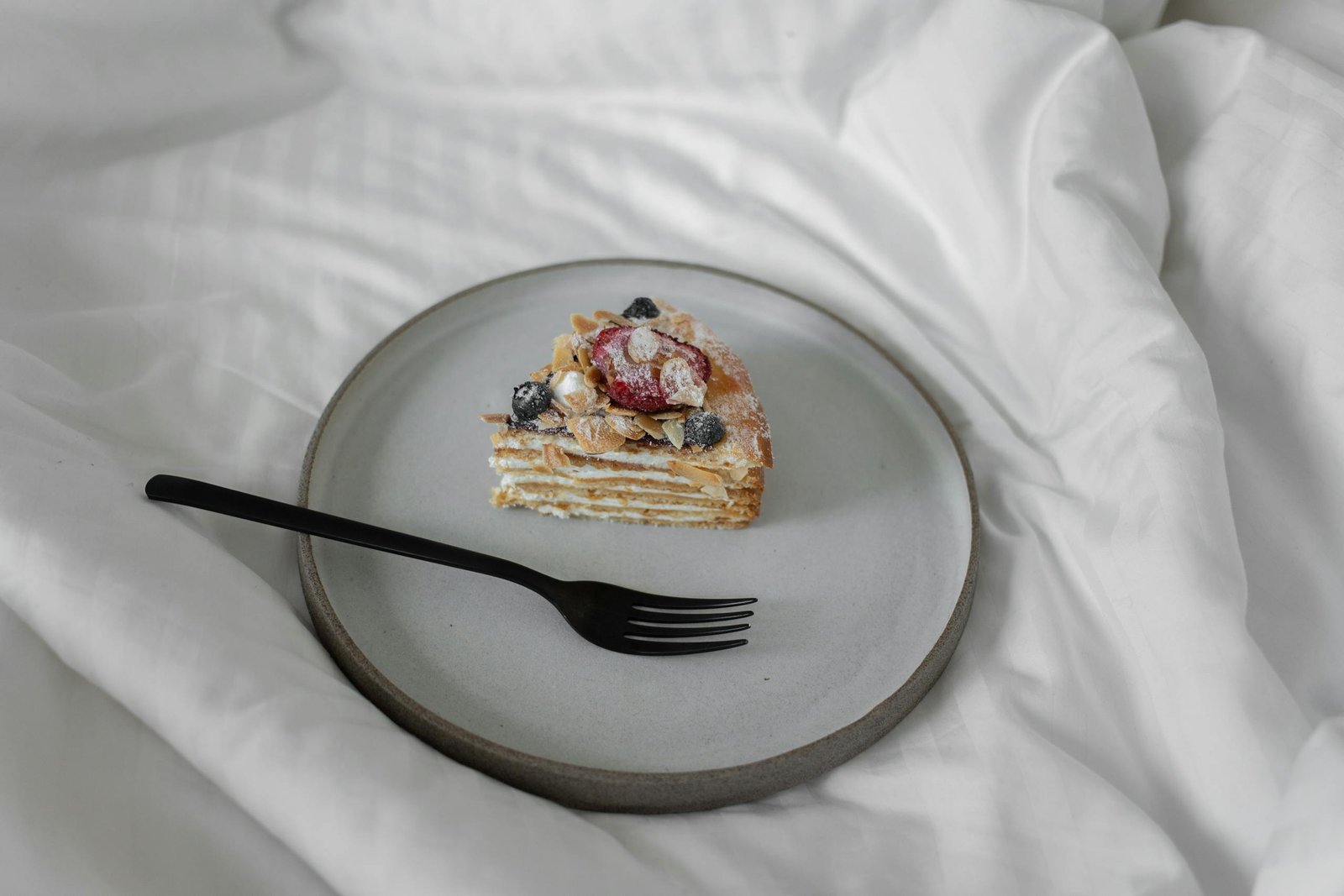 Delicious slice of layered cake topped with berries and almonds on a minimalist plate.