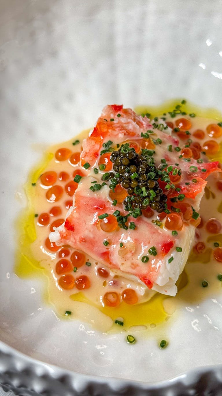 Elegant seafood dish featuring caviar and red roe, garnished with herbs.