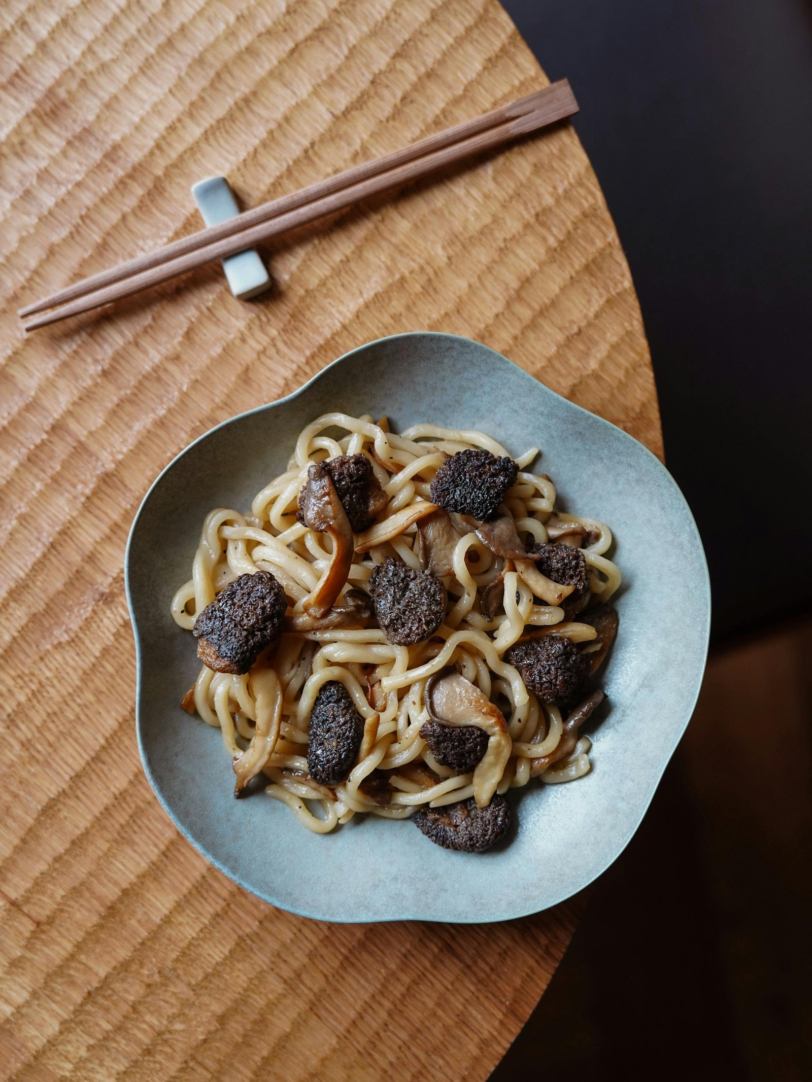 Top view of udon noodles with truffles and mushrooms on a wooden table, accompanied by chopsticks.